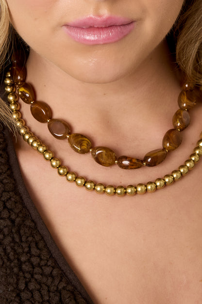 Detail shot of layered brown and gold beaded necklaces on woman wearing dark brown top