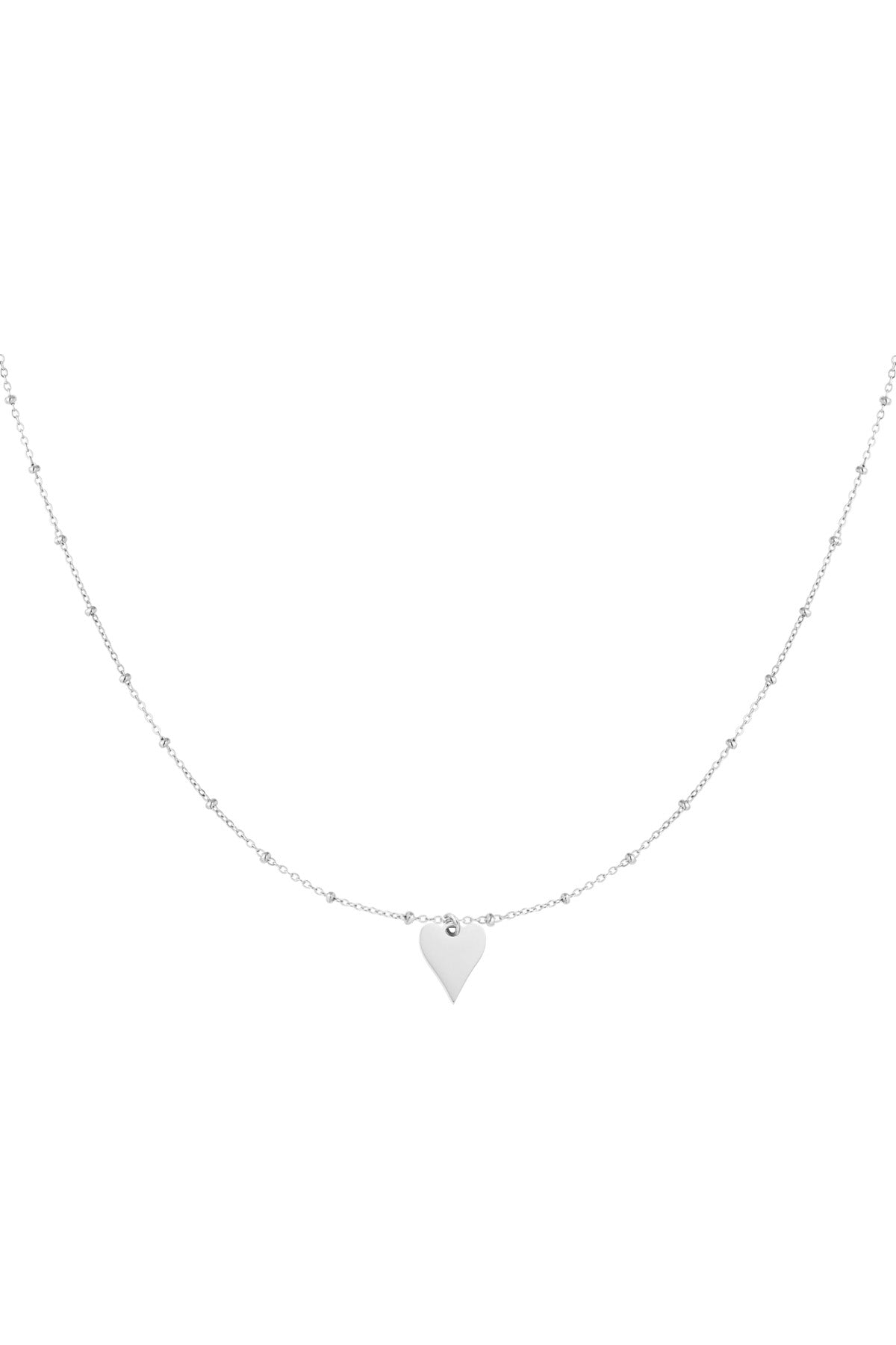 Close-up of delicate silver chain necklace with tiny beads and a small polished heart pendant.