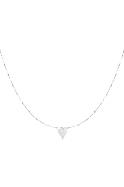 Close-up of delicate silver chain necklace with tiny beads and a small polished heart pendant.