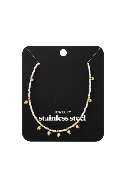 Delicate beaded necklace with tiny golden bells displayed on black jewelry card labeled stainless steel