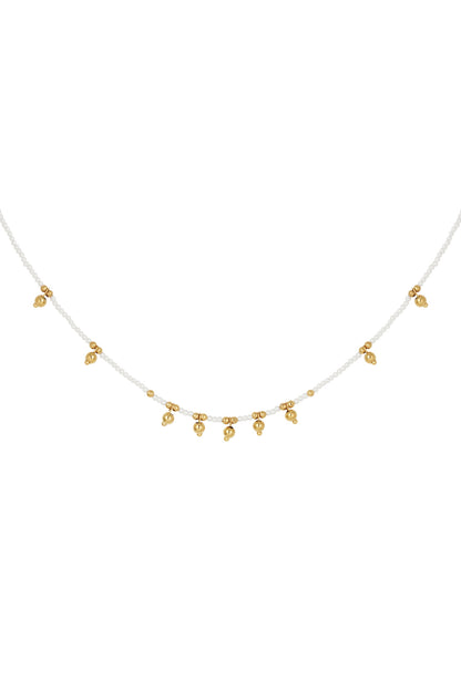Close-up of delicate beaded necklace featuring small white beads and evenly spaced gold bell charms on a white background