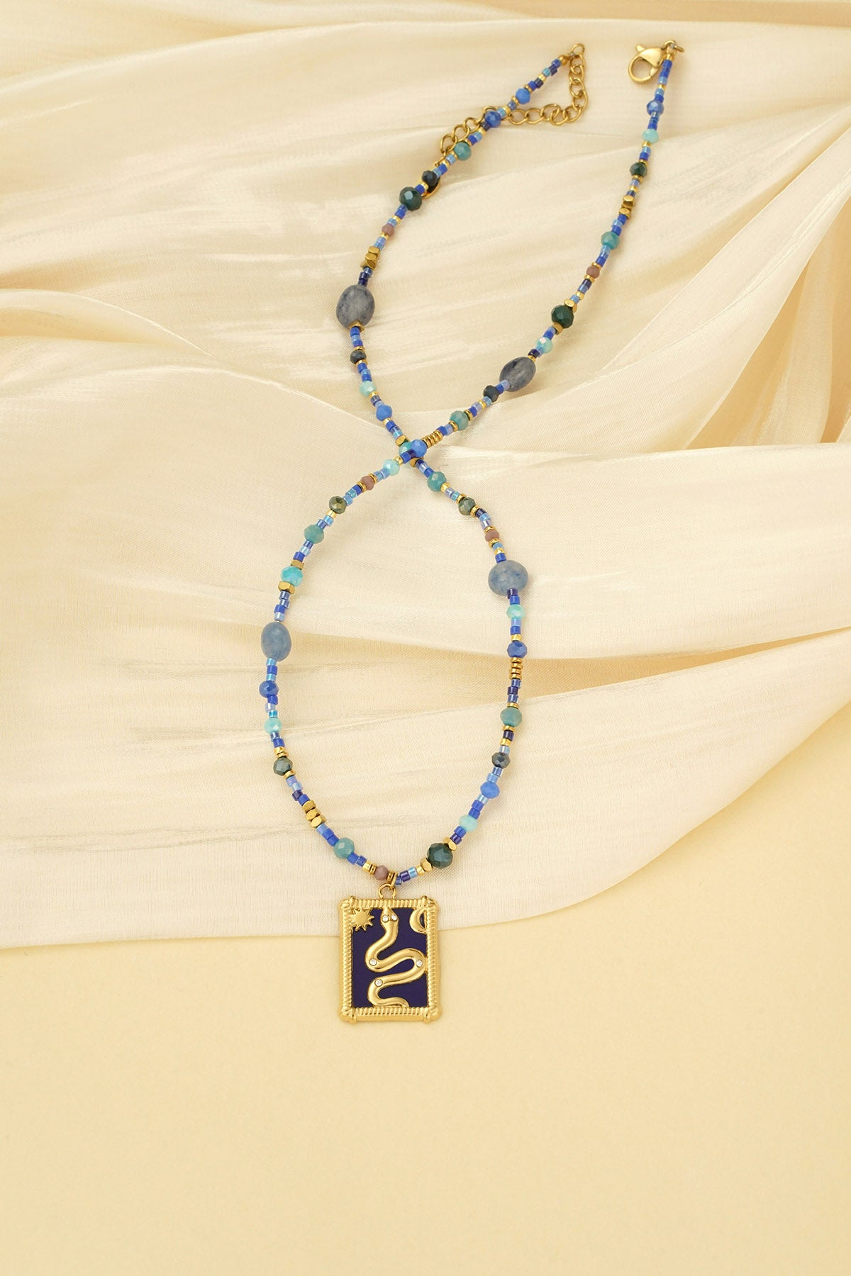 Blue beaded necklace laid on cream fabric, highlighting the gold snake pendant and bead details