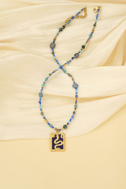Blue beaded necklace laid on cream fabric, highlighting the gold snake pendant and bead details