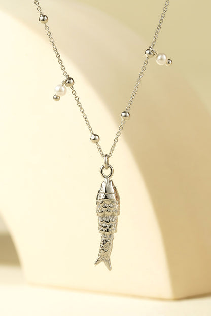 Detailed close-up of silver fish pendant and pearl bead chain against a beige background