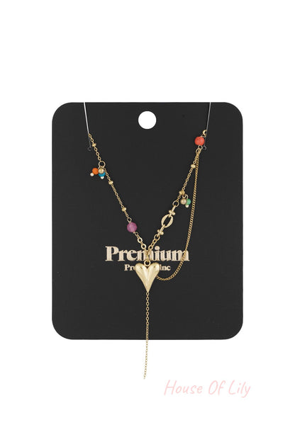 Gold heart pendant necklace displayed on black card with colourful bead accents and hanging chain detail