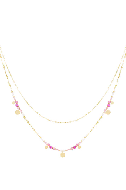 Double layered necklace with gold chains and pink lilac beads adorned with small gold sunburst charms on a white background