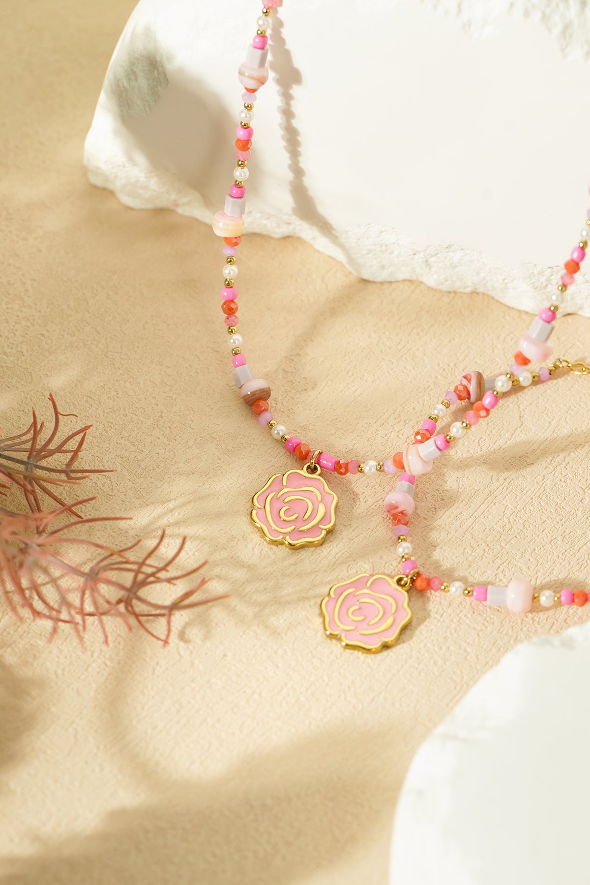 Two pink rose charm beaded bracelets styled on beige textured surface