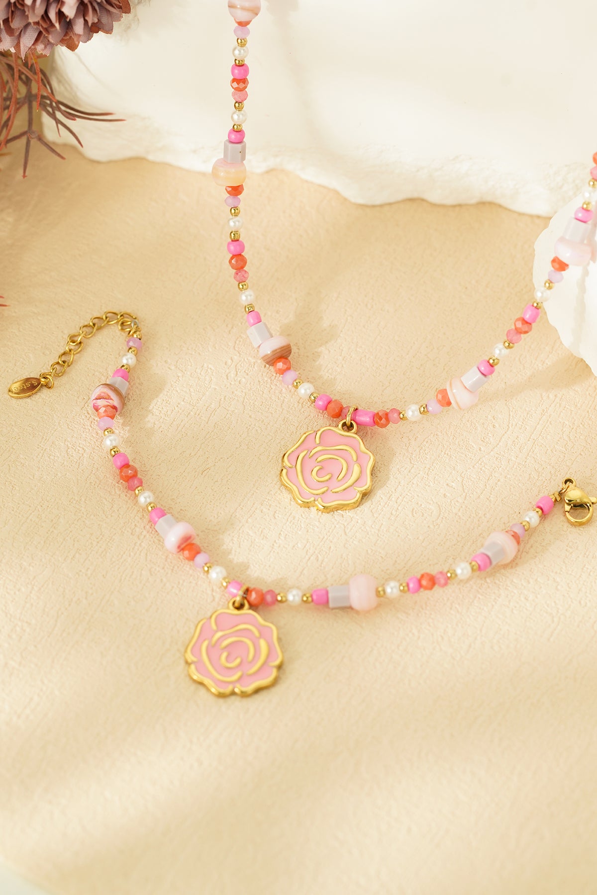 Pair of pink and coral beaded bracelets with gold rose charms close-up on beige background