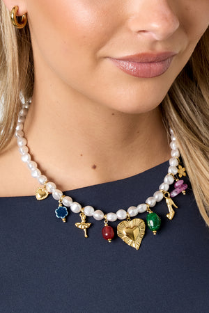 Close-up of a woman wearing the pearl charm necklace over a navy blue top, showing the necklace's colorful gold-tone charms