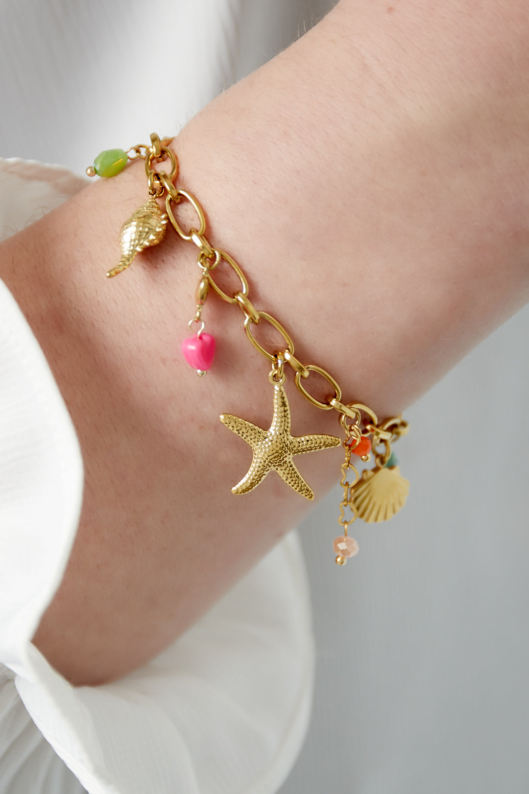 Close-up view of gold-tone sea charm bracelet worn on wrist with starfish charm and colorful bead accents
