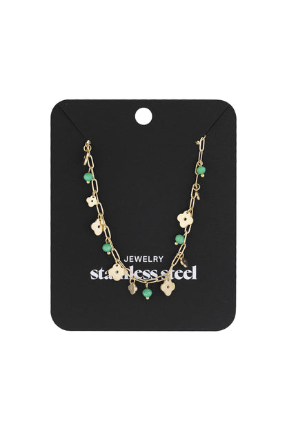 Gold-tone necklace with clover charms and green beads displayed on black stainless steel jewellery card
