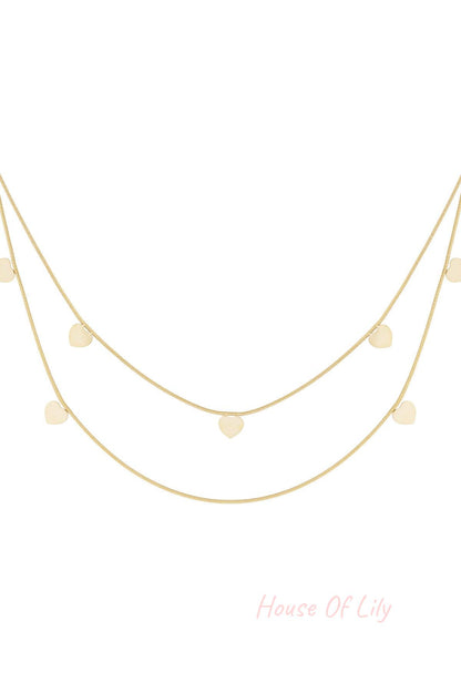Gold layered necklace featuring two fine chains adorned with small heart-shaped charms on a white background