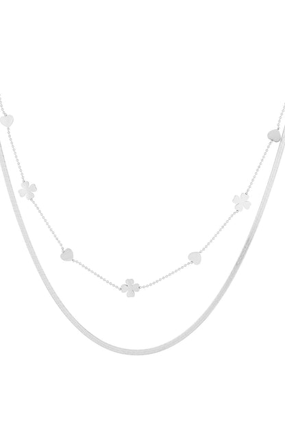 Close-up of silver double-layered necklace with heart and four-leaf clover charms on white background