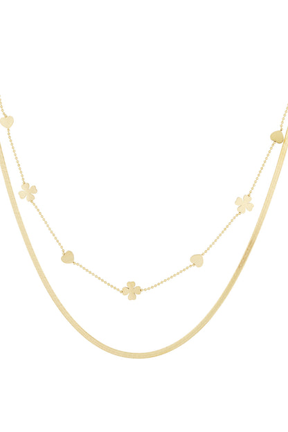 Close-up of gold double-layered necklace with heart and four-leaf clover charms on white background