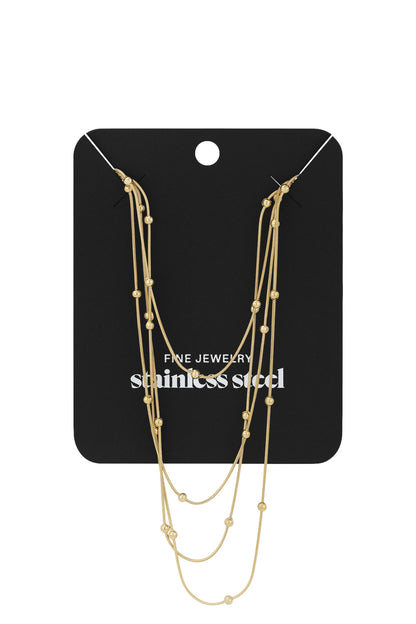 Layered gold beaded necklace displayed on black jewelry card labeled stainless steel