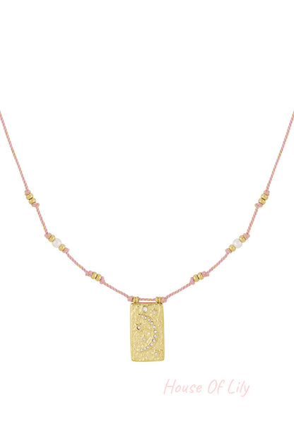 Close-up of a pink braided necklace with gold-tone moon pendant and crystal accents