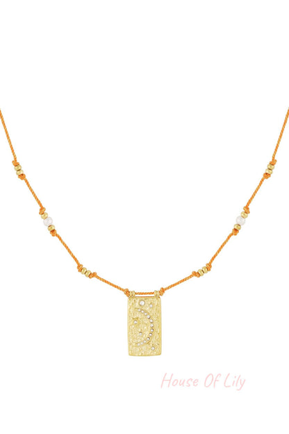 Flat lay of orange pendant moon necklace showing gold and pearl accents
