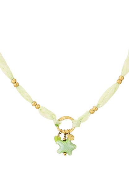 Close-up of soft green organza fabric necklace with matte gold beads and sea star charm with shell and heart pendants