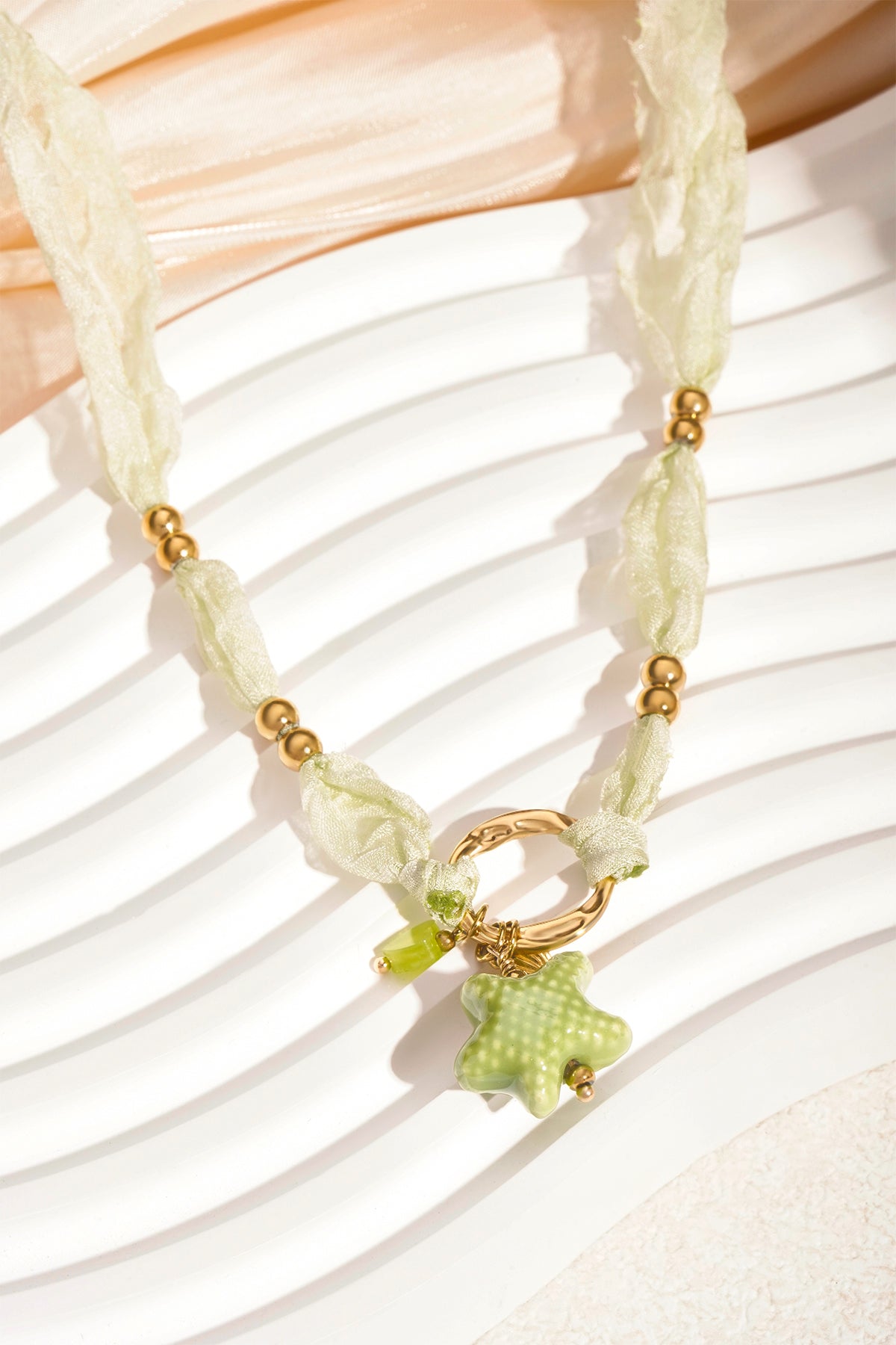 Sea star necklace with soft green fabric, gold beads, and dangling charms displayed on white textured surface