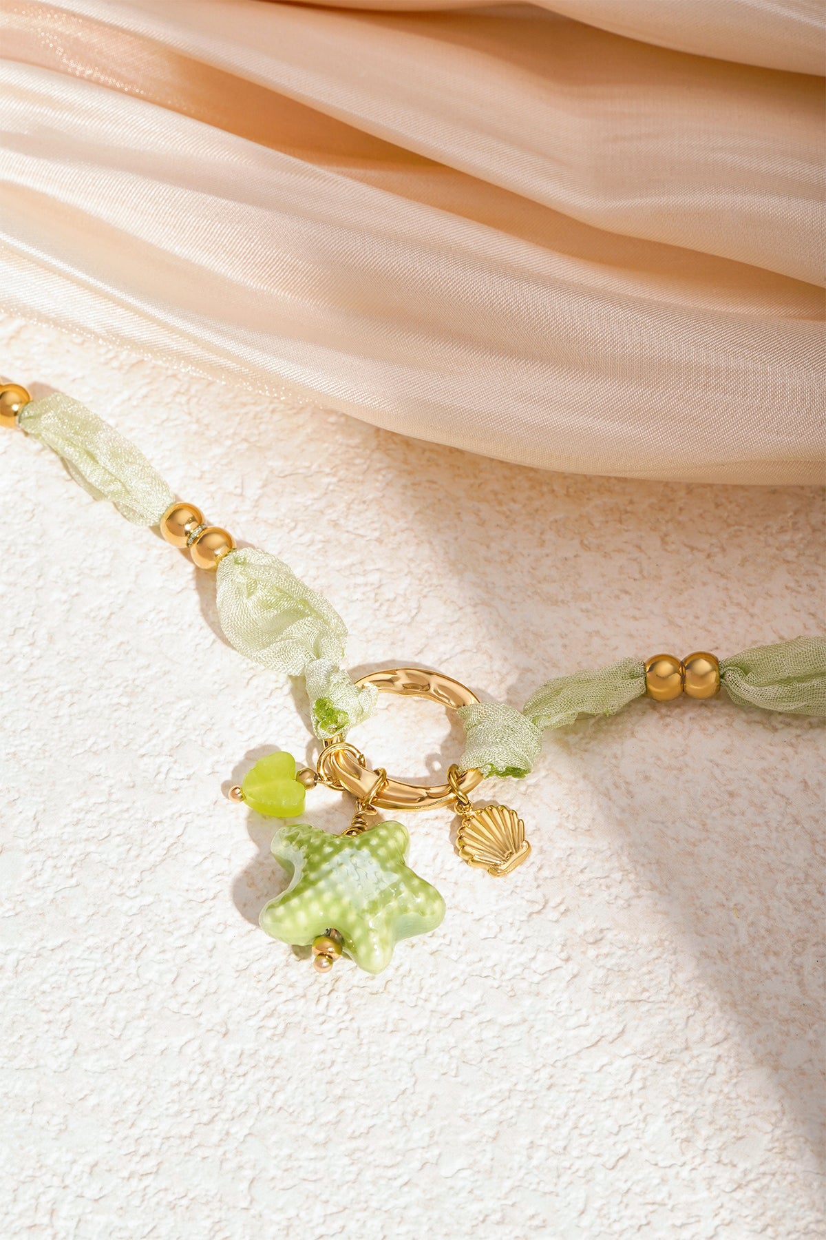 Close detail of necklace showing the soft knotted fabric, gold beads, and sea star charm on light background