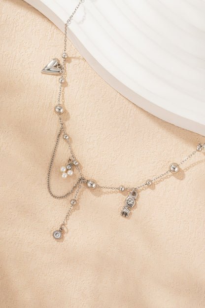 Close-up of silver tone charm necklace with pearl accents, LOVE pendant, and dangling chain on peach background