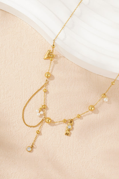 Detailed photo of gold charm necklace showing pearl cluster, LOVE pendant, heart and crystal drop on peach textured surface
