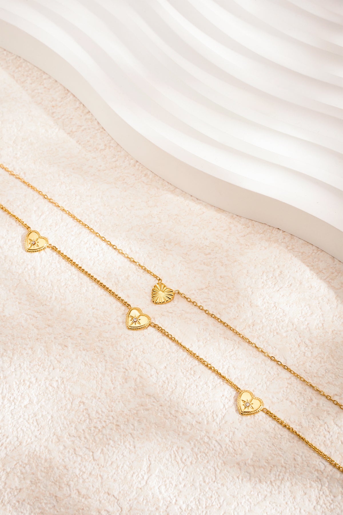 Gold-tone double layered necklace displayed on a textured surface with white sculptural background