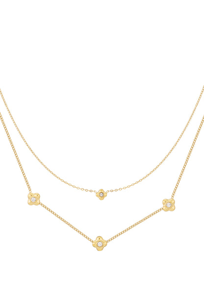 Close-up of delicate gold tone layered necklace with flower-shaped rhinestone accents on white background