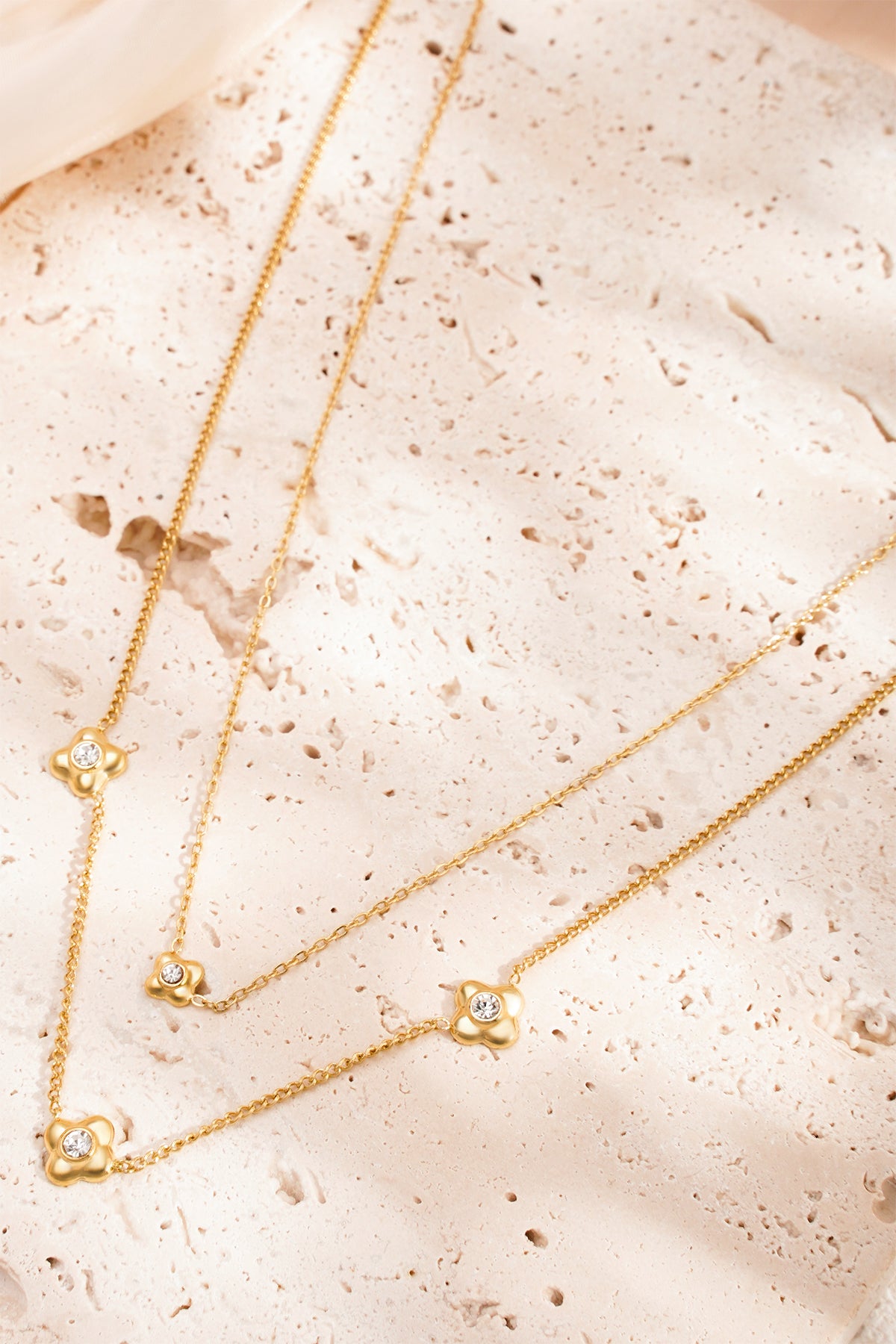 Gold tone layered flower necklace styled on natural textured stone surface showing chain and rhinestone detail