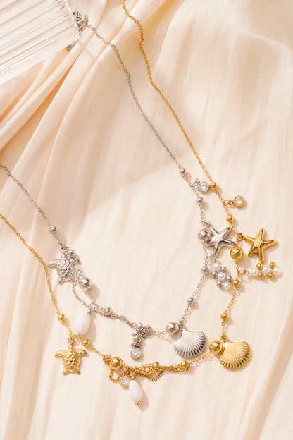Two ocean charm necklaces, gold and silver, laid on cream fabric with natural light highlighting pearl and charm details