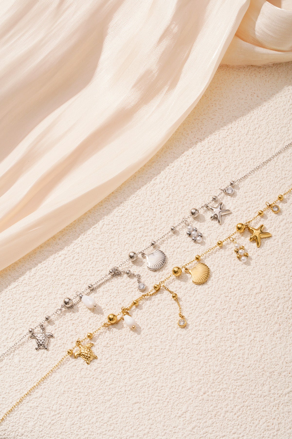 Pair of gold and silver ocean charm necklaces styled on cream textured surface highlighting detailed charms