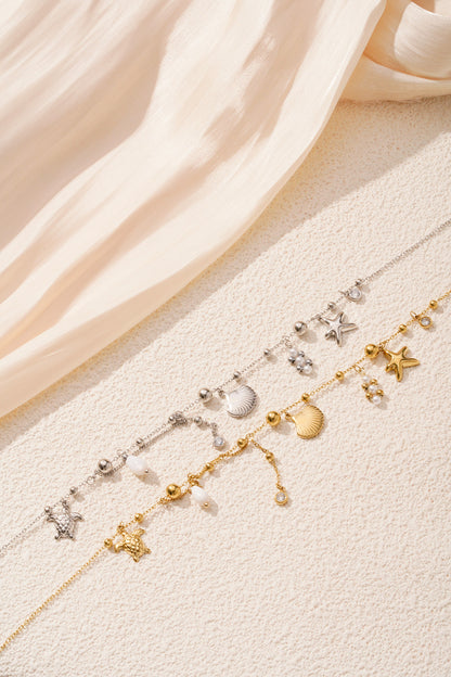 Pair of gold and silver ocean charm necklaces styled on cream textured surface highlighting detailed charms