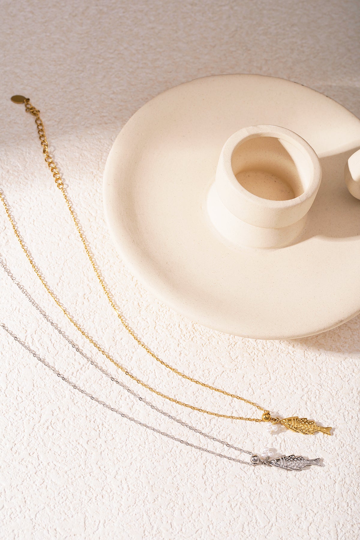 Gold fish pendant necklace with tiny pearl accents displayed on a cream candle holder