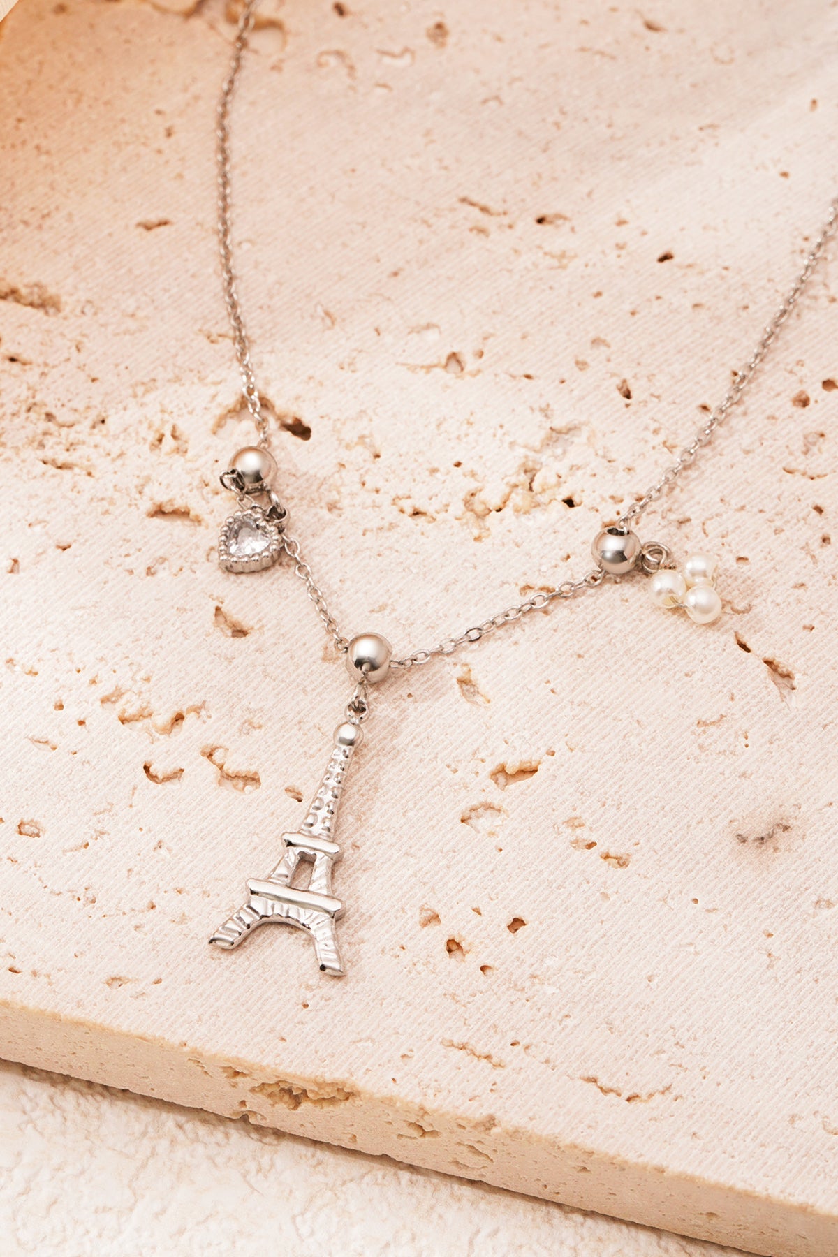Detail of gold and pearl heart charms on necklace chain on textured stone surface