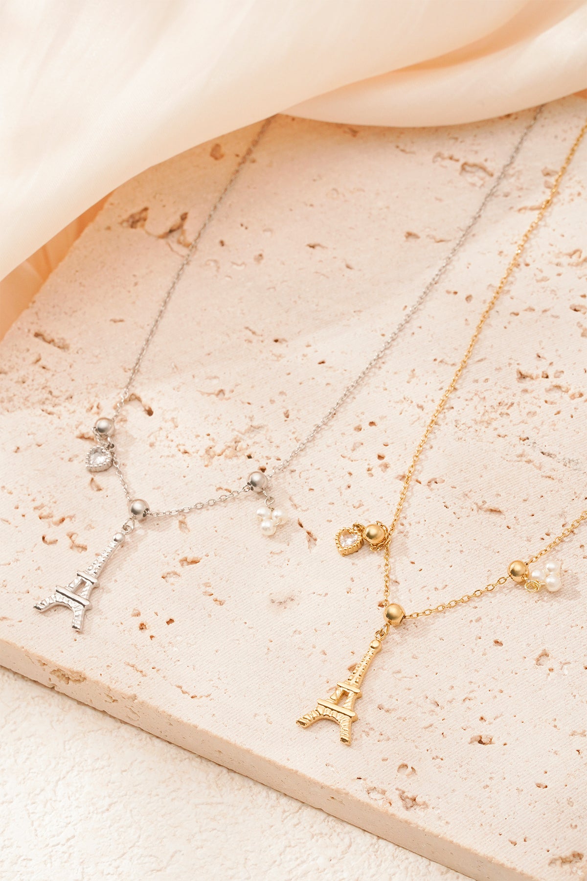 Silver Eiffel Tower charm necklace close-up on textured stone surface, featuring pearl cluster and heart charms