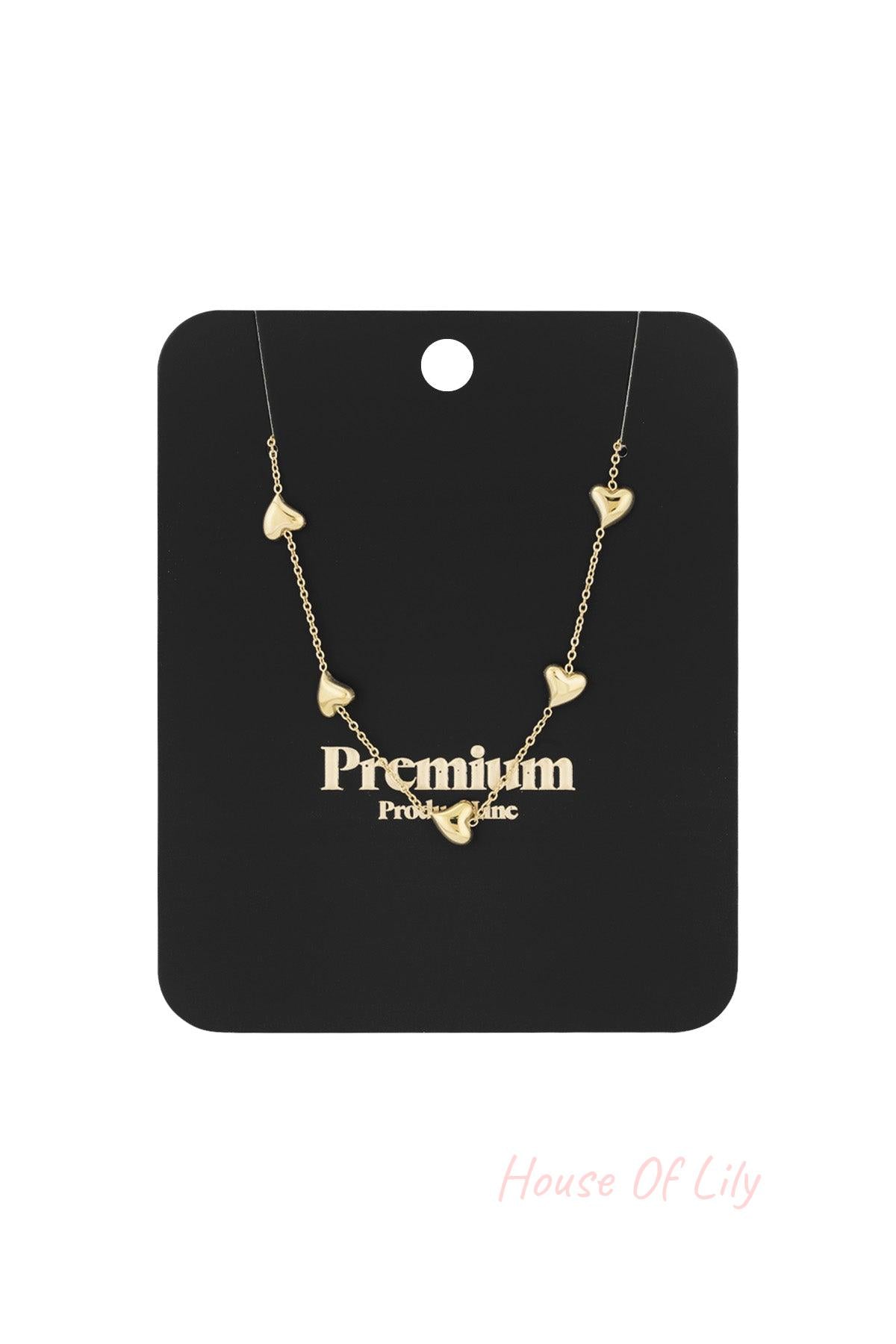 Gold heart charm necklace displayed on a black Premium product line packaging card