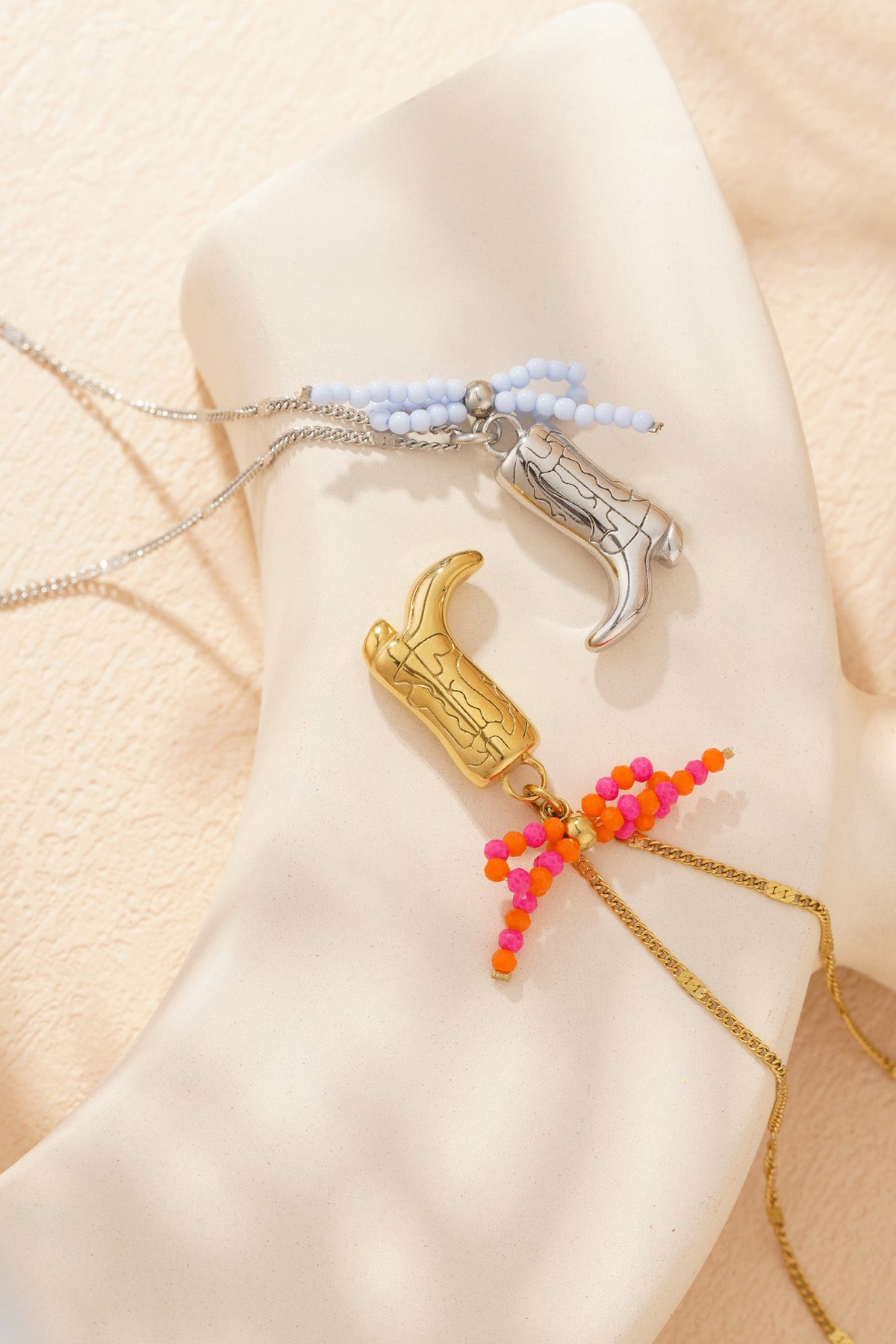 Close-up of silver-tone cowboy boot pendant necklace with pale blue beaded bow against cream background