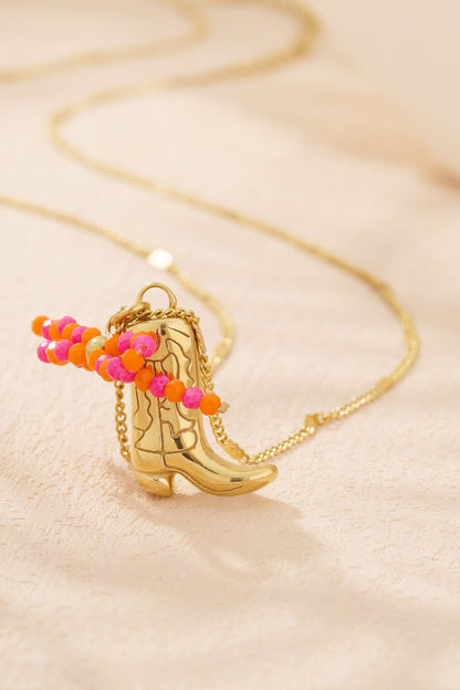 Close-up of gold-tone cowboy boot pendant necklace with pink and orange beads on cream background
