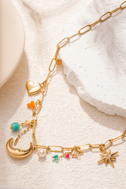 Detailed view of gold link chain necklace with moon, starburst and colourful charms on cream background