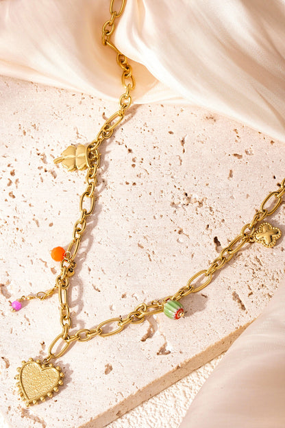 Golden charm link necklace placed artistically on a textured surface with soft fabric highlighting the necklace's colours and charms.