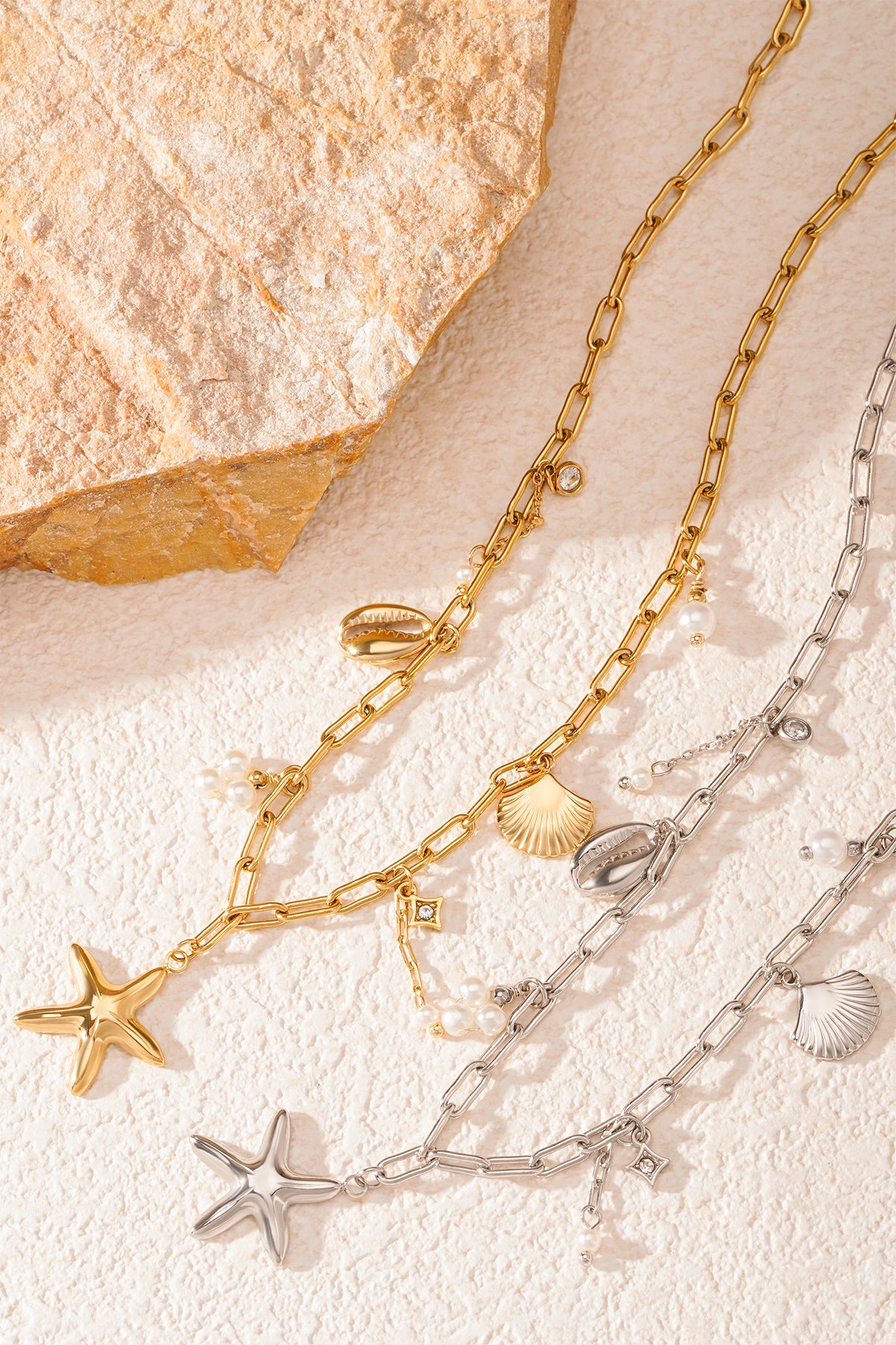 Gold and silver seaside charm necklaces displayed with natural stone props on textured surface