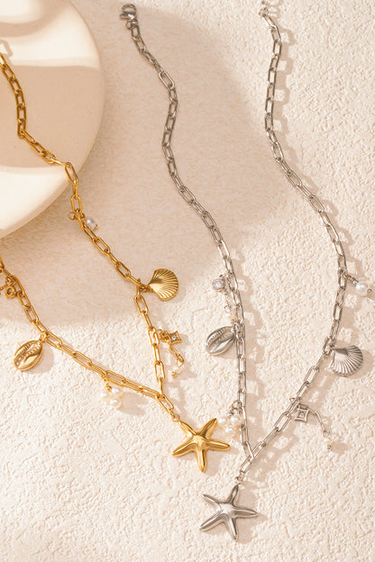 Gold and silver seaside charm necklaces laid flat on a textured white surface, showcasing starfish, shells and pearl clusters