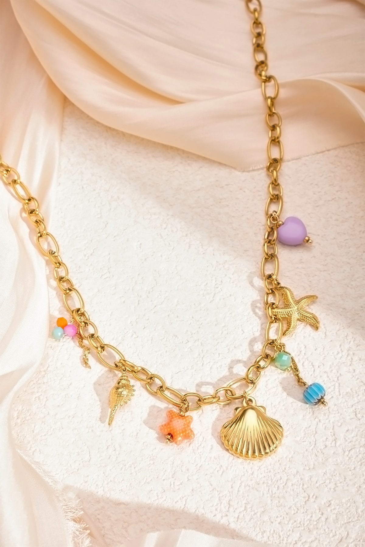 Styled shot of the necklace laid on a cream textured background showing the beach-themed charms