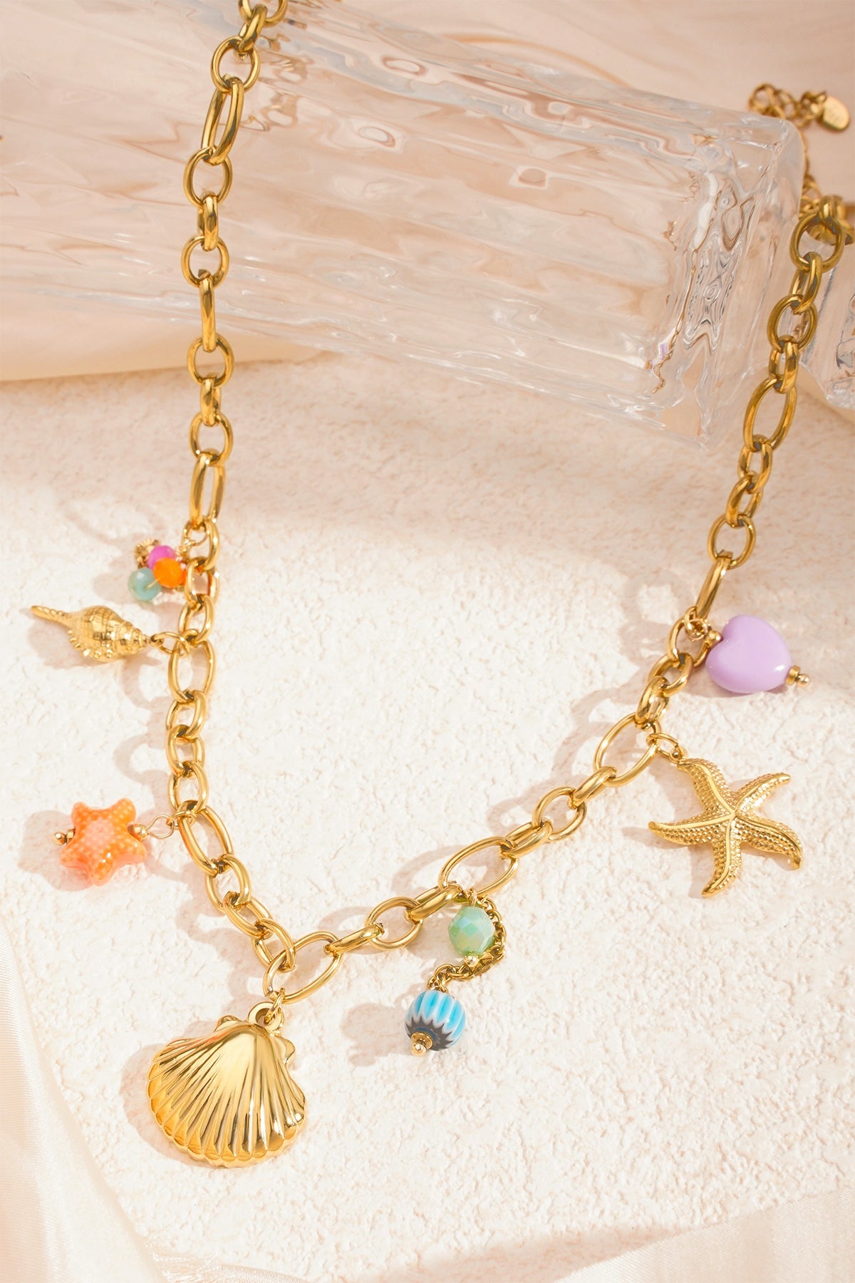 Close-up of sea charm necklace on textured surface with gold chain and multicoloured beads