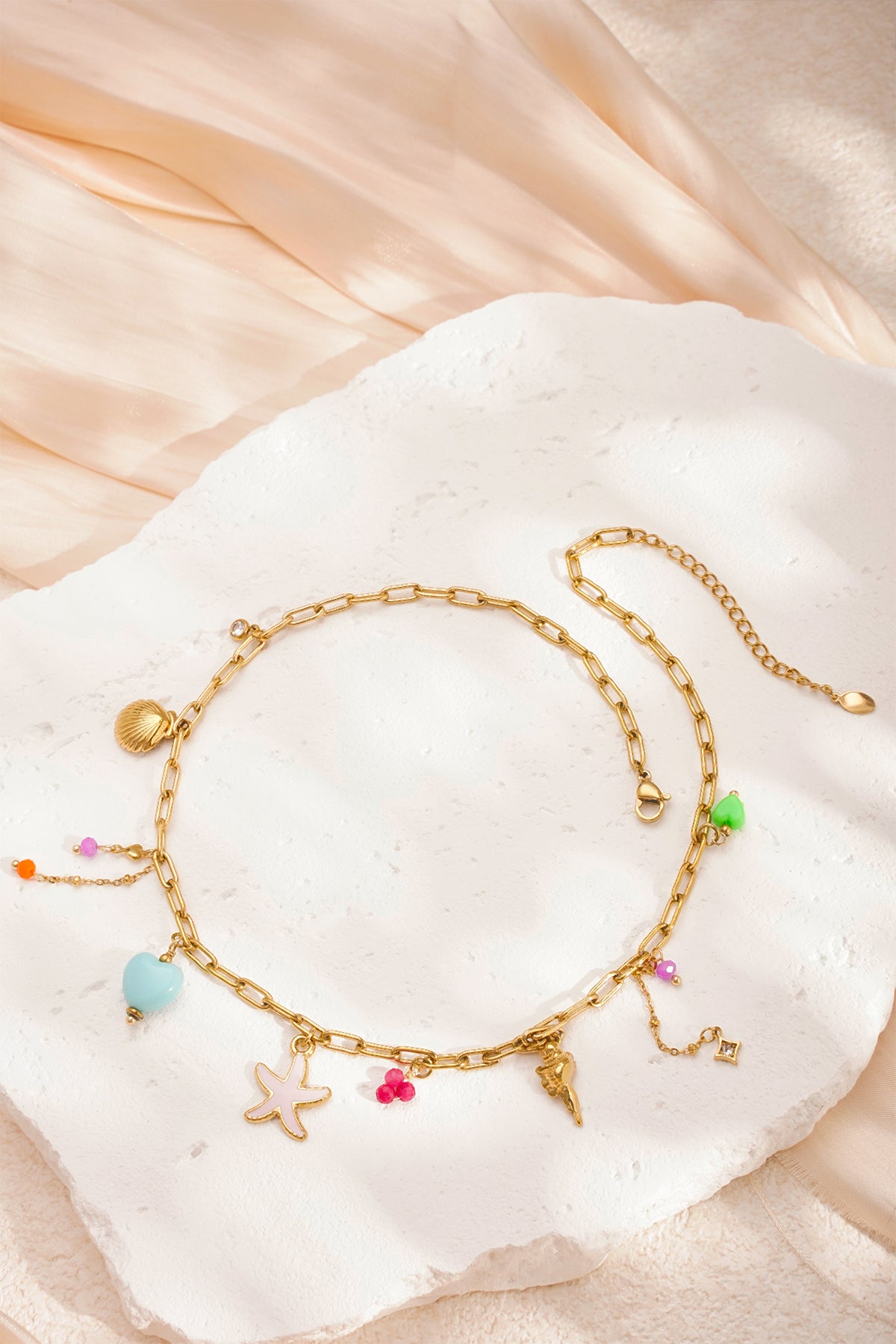 Flat lay of gold-tone charm necklace with starfish, seashells and bead charms on white textured display