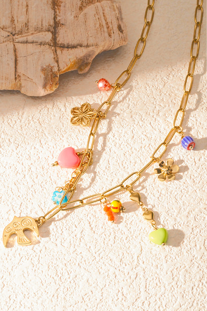 Soft natural light on gold chain necklace with bright playful charms arranged on textured cream surface