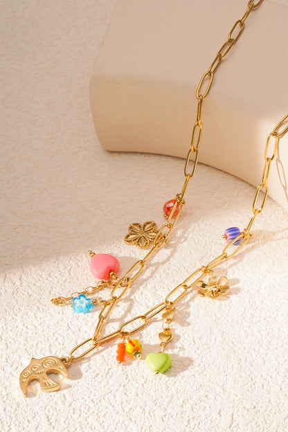 Detailed view of necklace on a light textured background showcasing intricate colourful and gold flower, heart, and bead charms