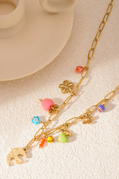 Close-up of necklace laid on textured surface highlighting colourful heart, flower, bird and bead charms on gold links
