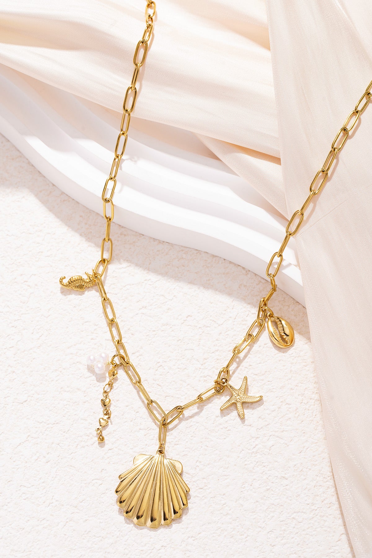 Close-up image of the gold charm necklace arranged elegantly on beige fabric highlighting the shiny shell and starfish charms.
