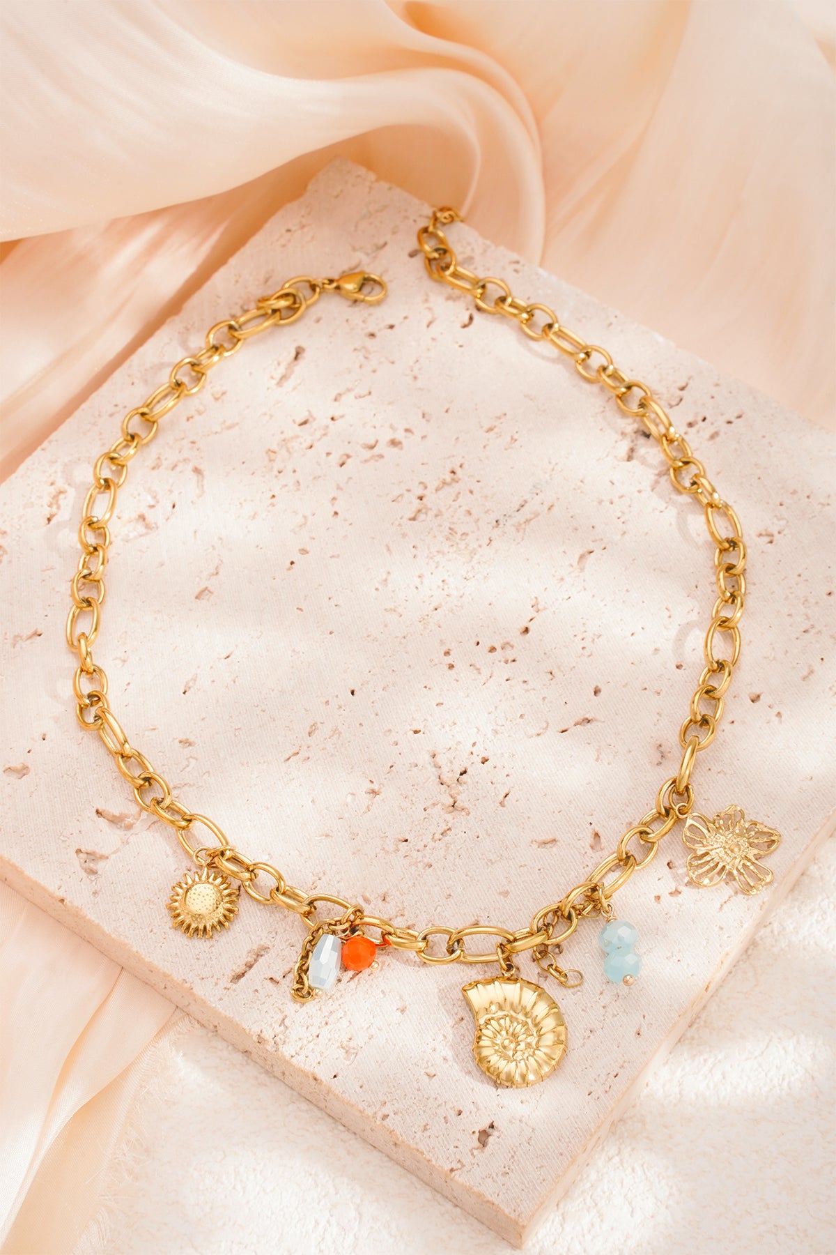 Close-up shot of gold charm necklace laid flat on a textured beige surface
